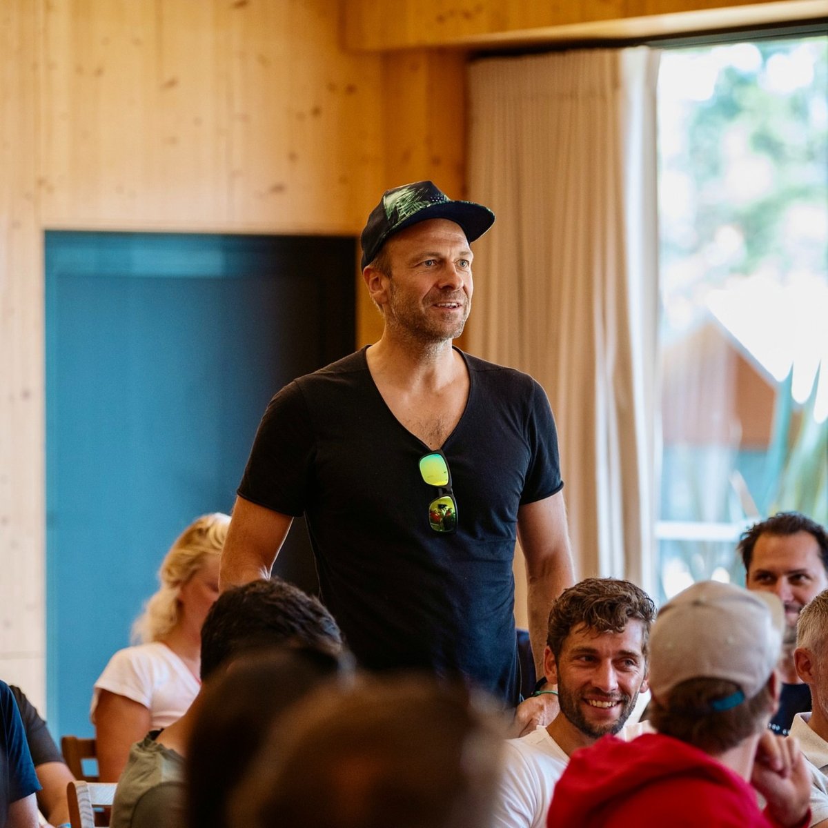 Johannes Herold wearing a cap, standing among seated participants of the Founders Kite Club in Viana