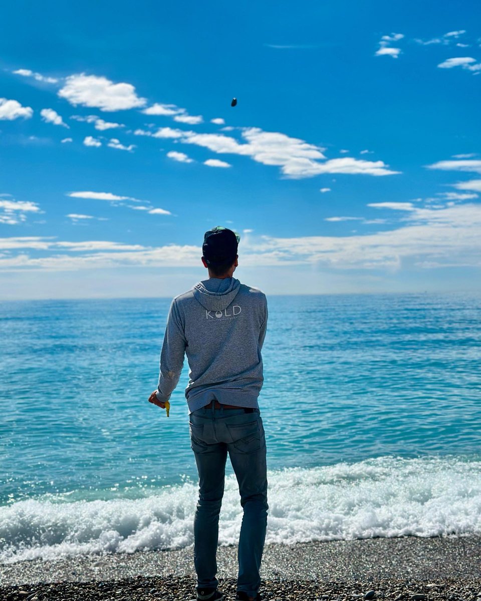 Johannes Herold stands with his back to the camera on the pebble beach in Nice, looking out at the sea