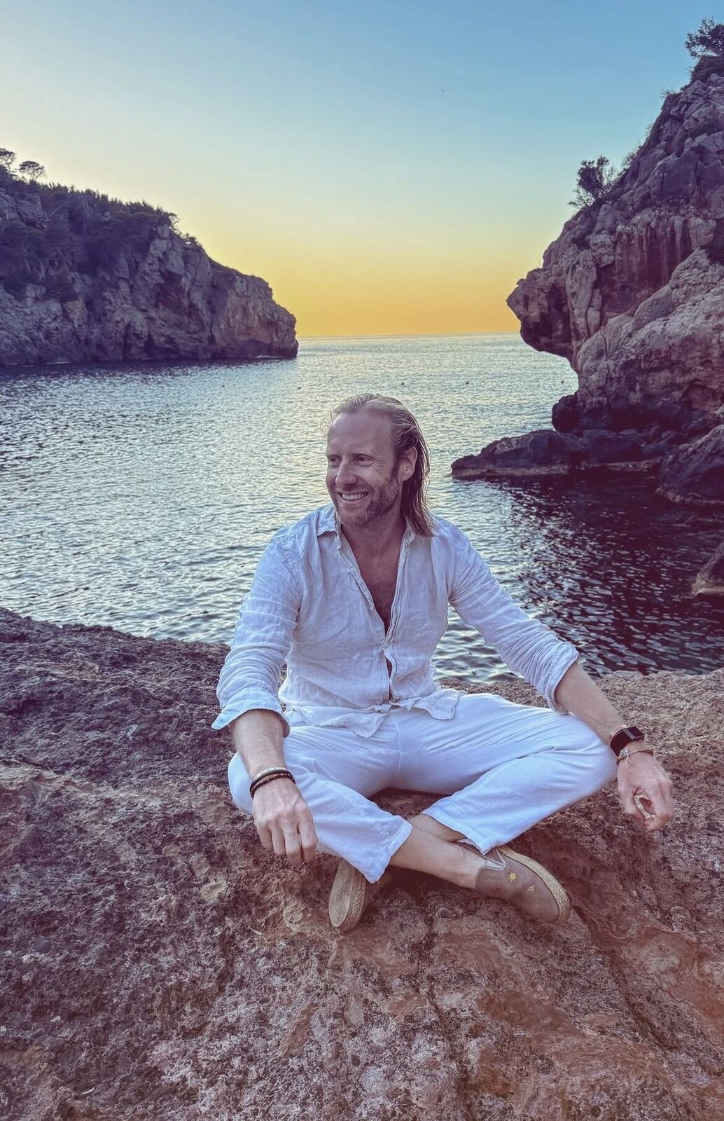 Sebastian Grote sitzt bei Sonnenuntergang auf einem Felsen in einer Bucht