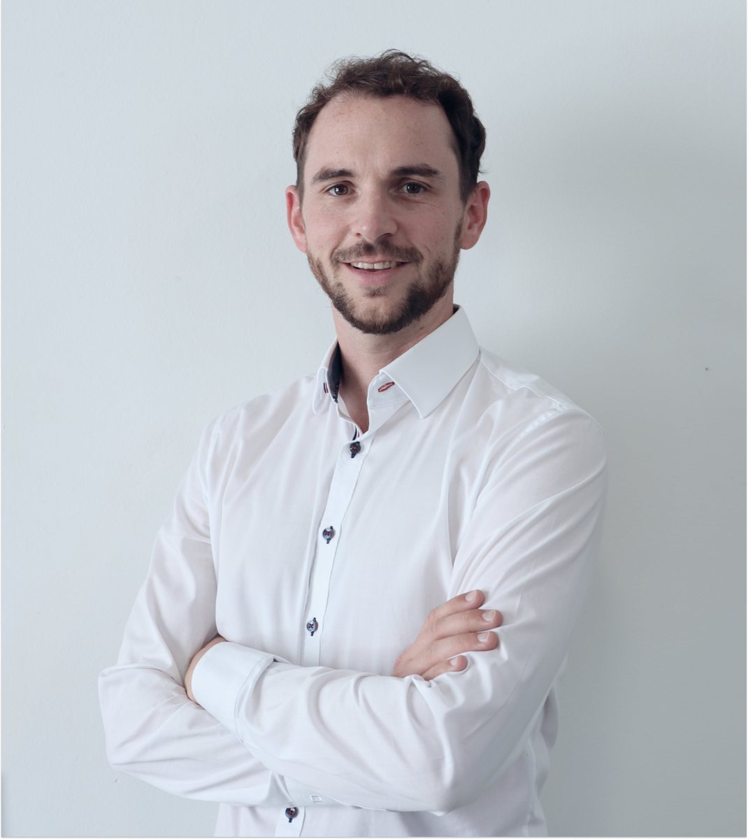 Tobias Kupke in a white shirt with arms crossed in front of a light gray background.