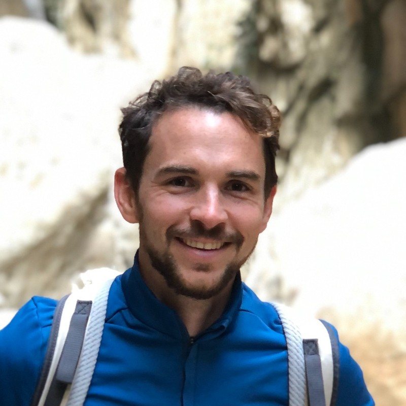 Tobias Kupke smiles in a blue technical jacket with a backpack in front of a rock face.